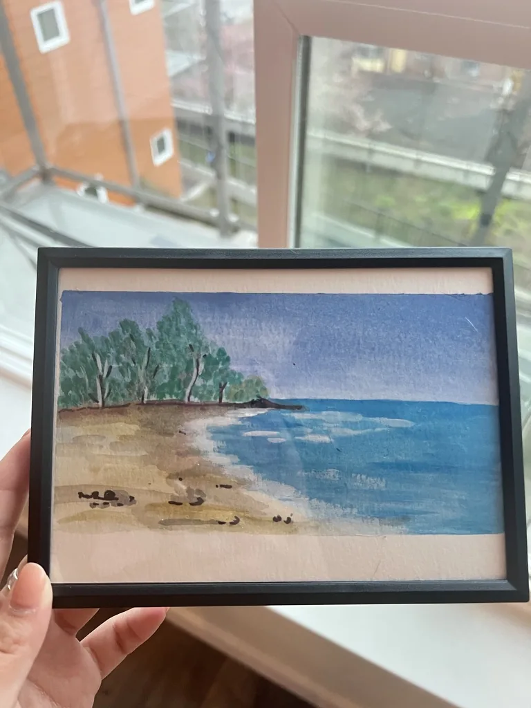 Small watercolor of a quiet beach with trees and blue water
